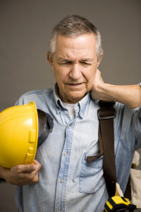 Construction worker with hardhat off rubbing his neck that is in pain.