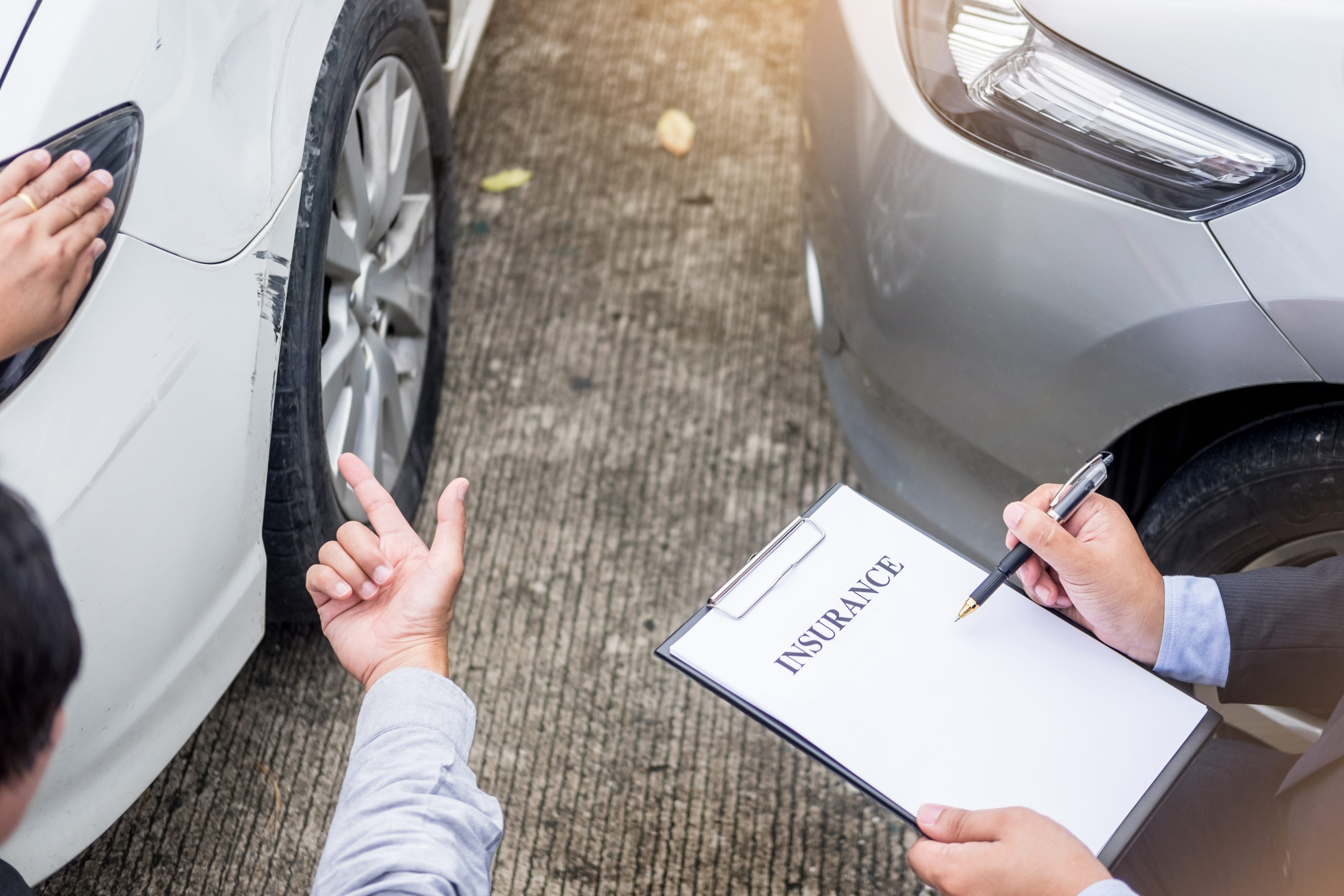 Insurance agent writing on clipboard while examining car