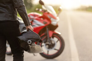 Handsome motorcyclist wear leather jacket and holding helmet on the road. Safe ride and transportation concept
